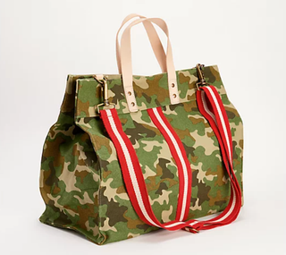 Oblique view of Venture Camo tote bag with red and white adjustable strap and stripe down the middle. With natural tan handles.