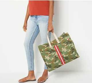 Woman holding Venture Camo tote bag with red and white adjustable strap and stripe down the middle. With natural tan handles.