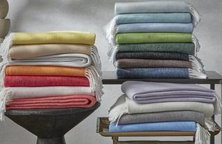 Stack of folded Matouk Pezzo throw blankets in all colors.