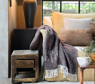 Sable colored, monogrammed throw blanket draped over the corner of a sofa.