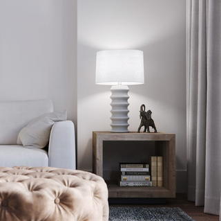 Off white/pale grey ceramic table lamp with a white tapered drum shade. Shown on a side table.