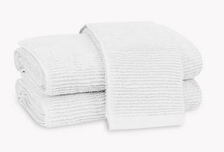 Stack of white, ribbed Matouk Aman towels. Two bath towels and one hand towel.