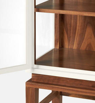 Made Goods Jamison Cabinet in pristine faux raffia and walnut veneer. Cabinet with glass dooes  in pristine faux raffia resting on tall walnut veneer legs. Close up view of interior and base detail.