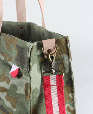 Close up of ShoreBags Venture Camo tote bag with red and white adjustable strap and stripe down the middle. With natural tan handles.