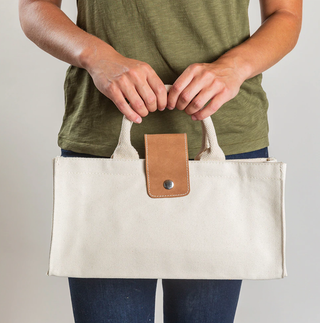 Woman holding ShoreBags Natural Canvas wine tote with natural handles and Tan Leather Tab with snap.