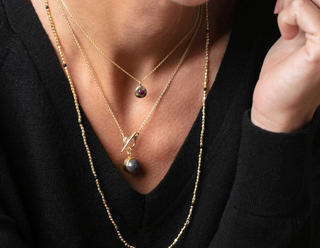Person wearing three necklaces including the longest gold beaded necklace with black beads