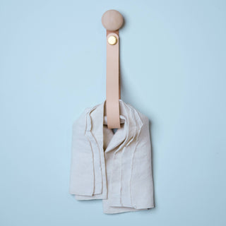 Wooden knob with natural leather strap attached and kitchen towel hanging through it.