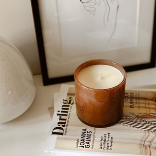 Brown handblown glass candle on top of newsprint in front of artwork