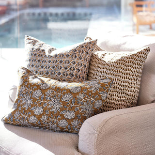 Self welted linen pillow in tobacco with off white and blue floral patter with two other pillows on a outdoor chair by the pool